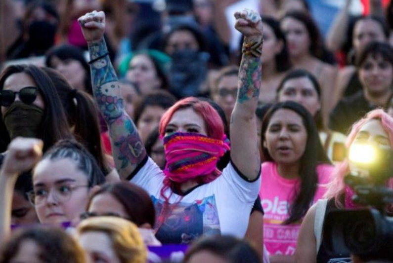 Mujeres feministas radicales con los brazos en alto, mostrando su compromiso con la igualdad de género y la lucha contra la opresión. Las mujeres parecen estar coreando lemas y mirando hacia el mismo lugar